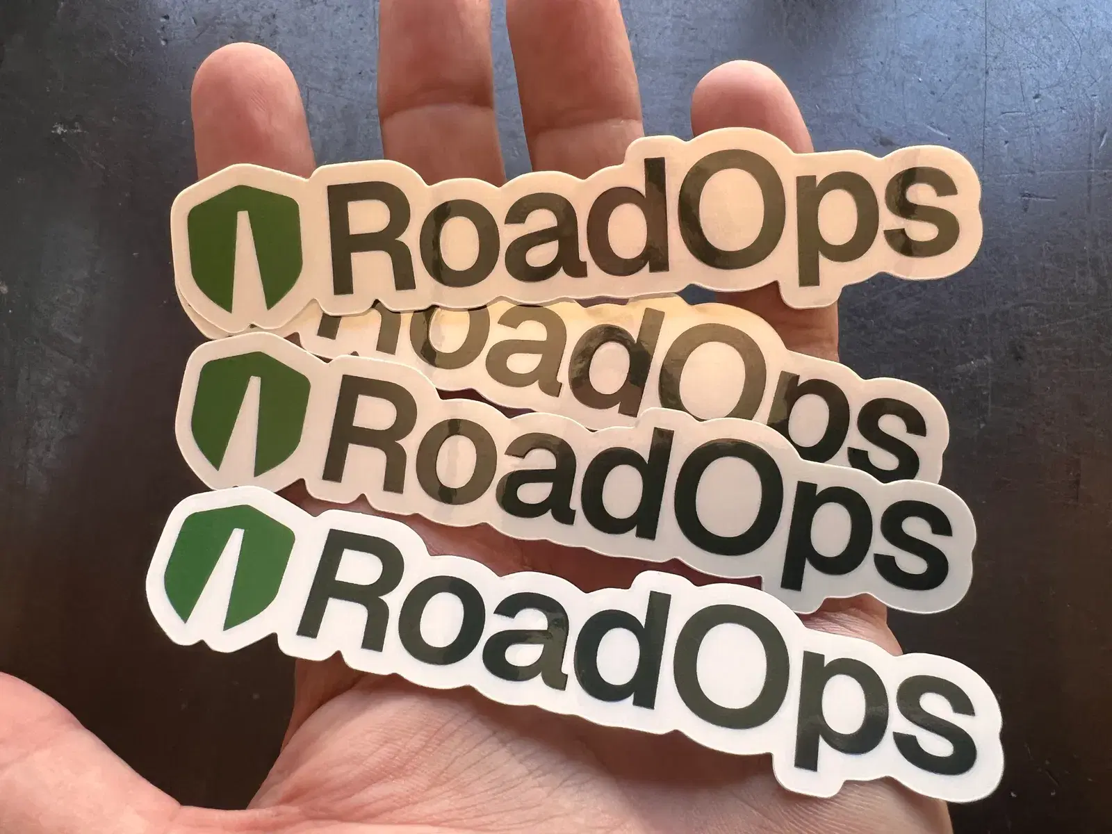 A hand holding white die-cut RoadOps logo stickers.
